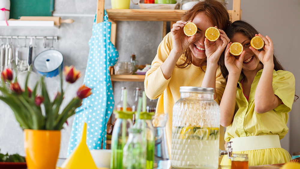 Mother and daughter goofing around in a colorful kitchen with lemons covering their eyes
