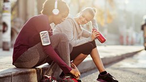 Two young women sitting on a curb getting ready to do a workout