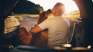 A man sitting in the back of his car with the trunk open warmly embracing his dog