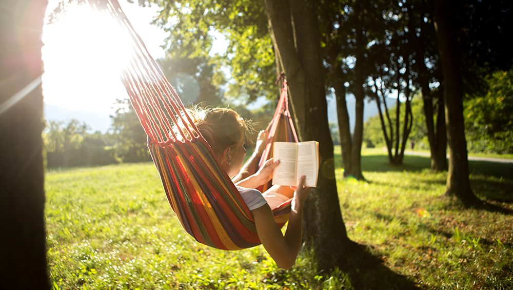 Woman on hammock at sunset reading book