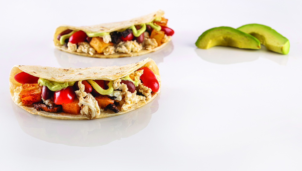 Two tacos filled with egg whites, potatoes, mushrooms, tomatoes and avocado sauce