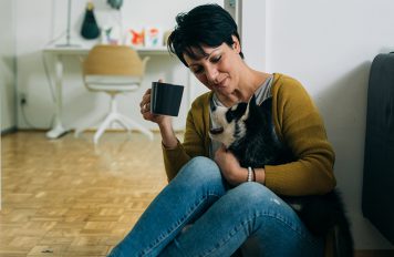 Woman drinking tea and playing with her puppy at home